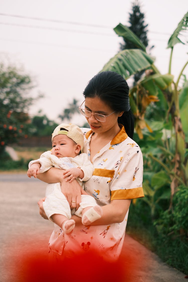 Young Asian Woman In Glasses With Baby In Summer Garden