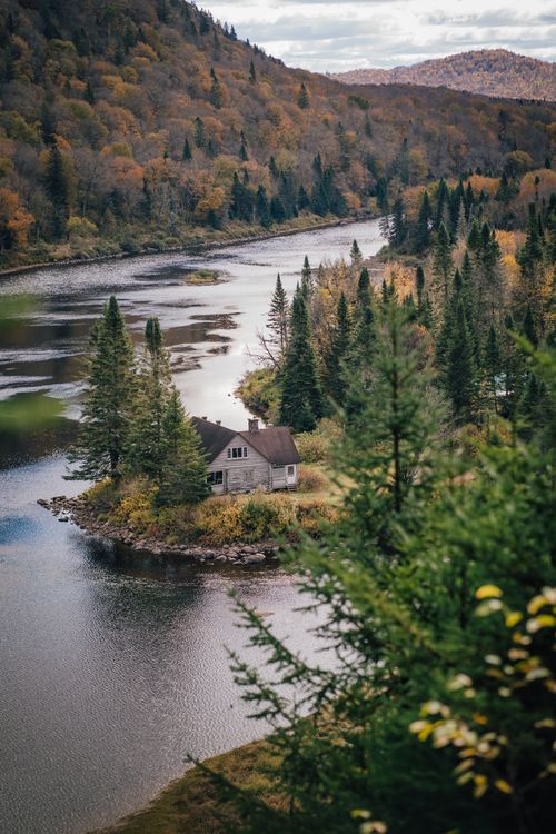 Free Charming house nestled by a river in a vibrant autumn forest, perfect for tranquil travel retreats. Stock Photo