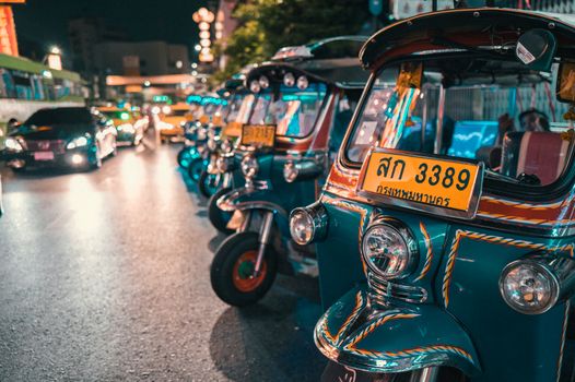 Vibrant row of tuk-tuks at night, illuminating the busy Thai city streets.