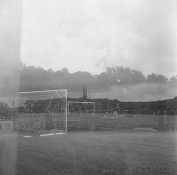 Artistic double exposure of a foggy soccer field with goal post and distant landscape.