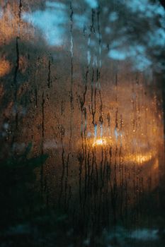 A window with rain droplets and warm light reflections creating a moody and calming atmosphere.