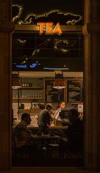 Warm indoor café setting at night with patrons and barista interacting, creating a relaxed atmosphere.