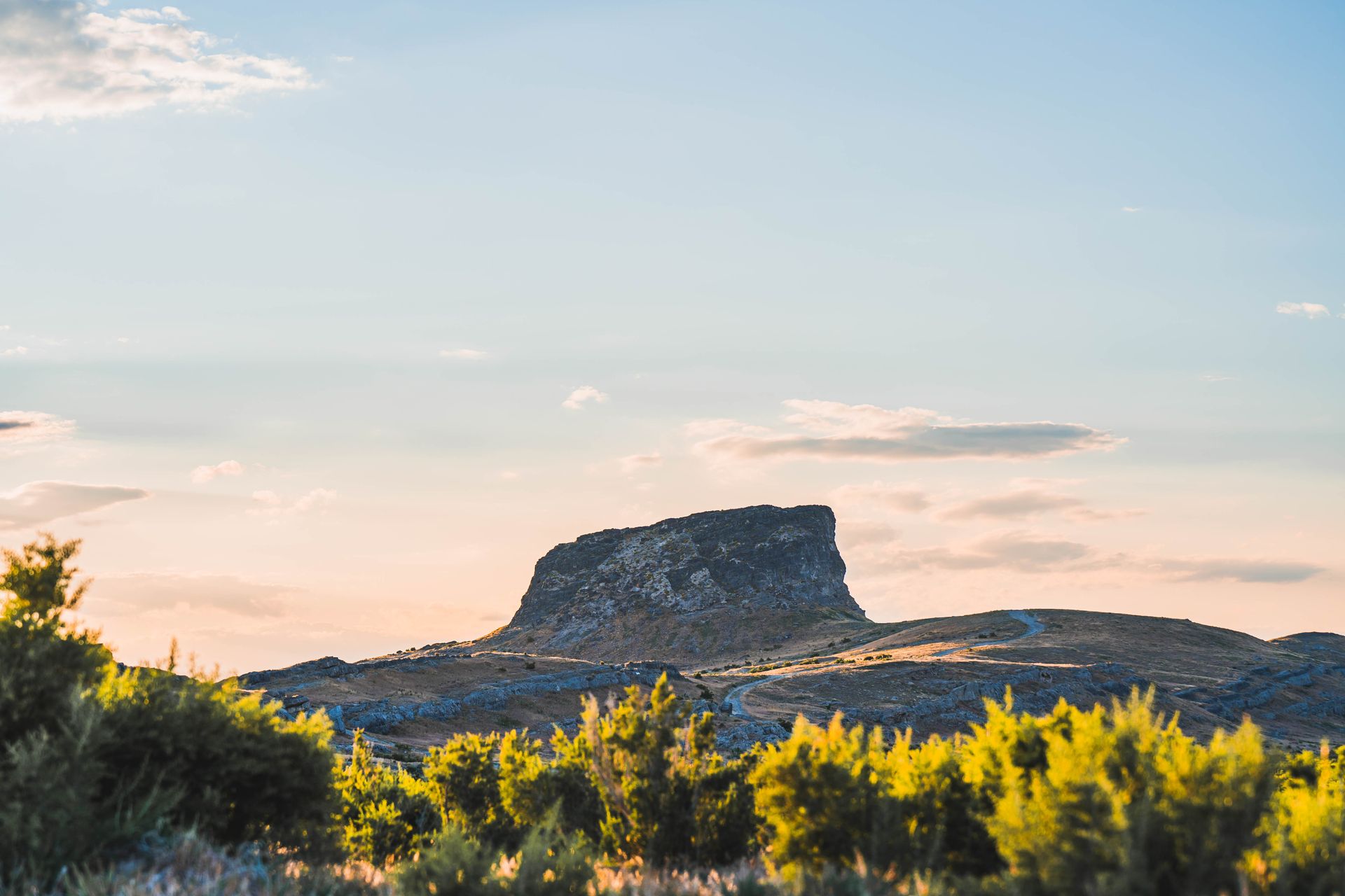 A breathtaking view of a rocky mesa under a serene sunset, surrounded by open land.