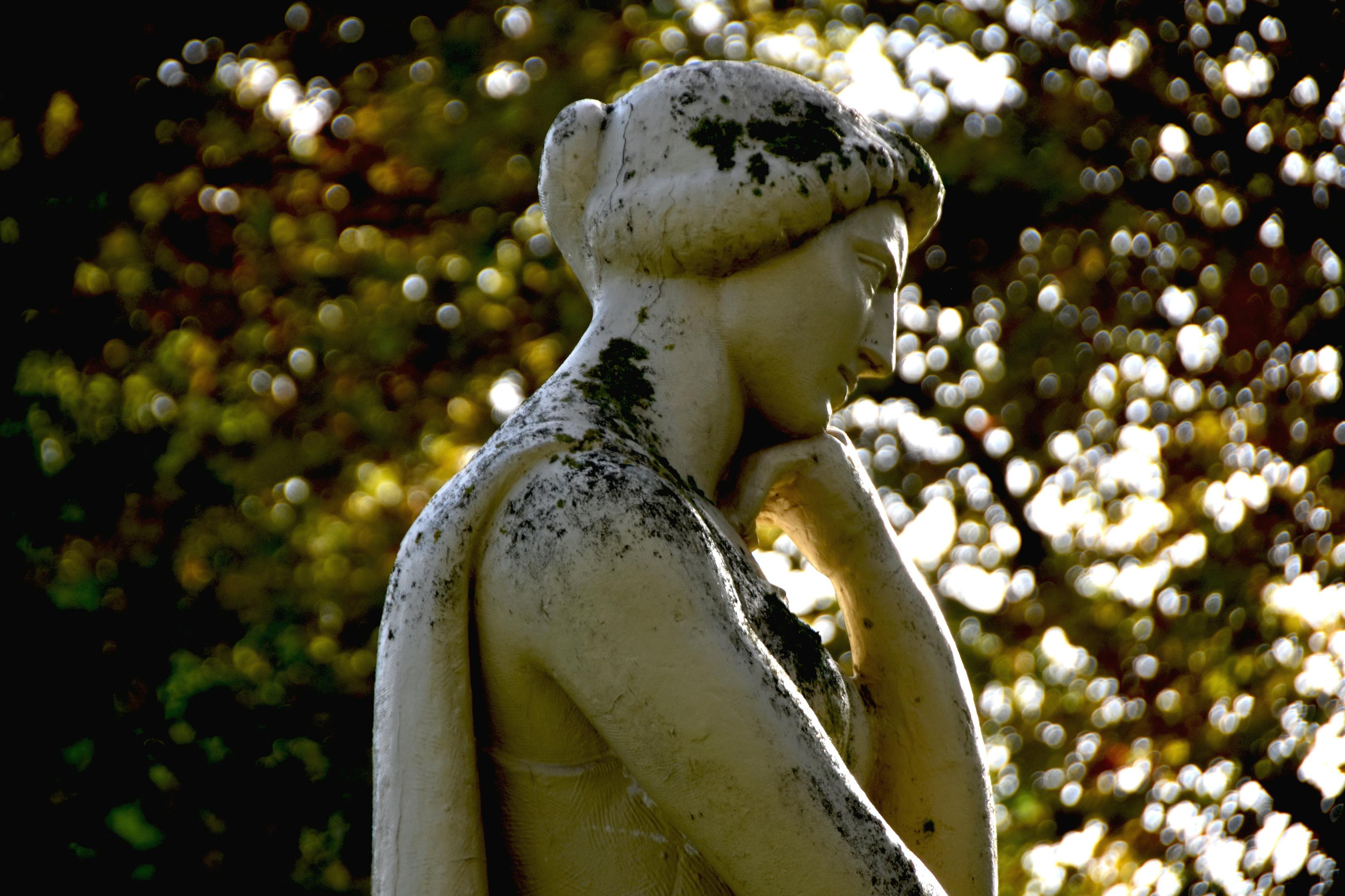 Close-up of a moss-covered marble sculpture in a Lisbon park under dappled sunlight.
