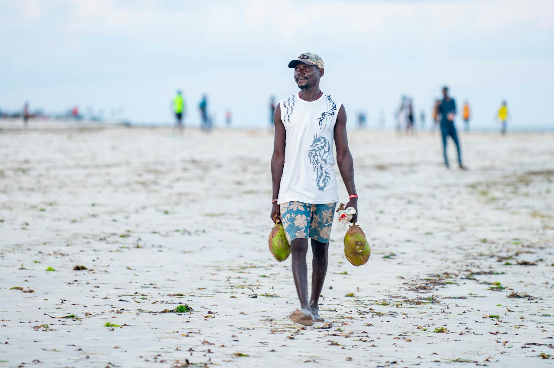 Man strolling on Mombasa beach carrying coconuts, showcasing a laid-back lifestyle.