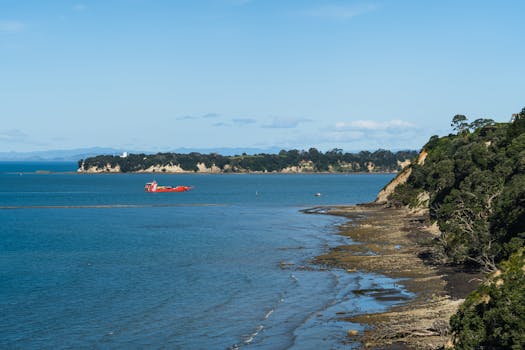 Stunning coastal view of Auckland with a red ship, blue skies, and lush greenery.