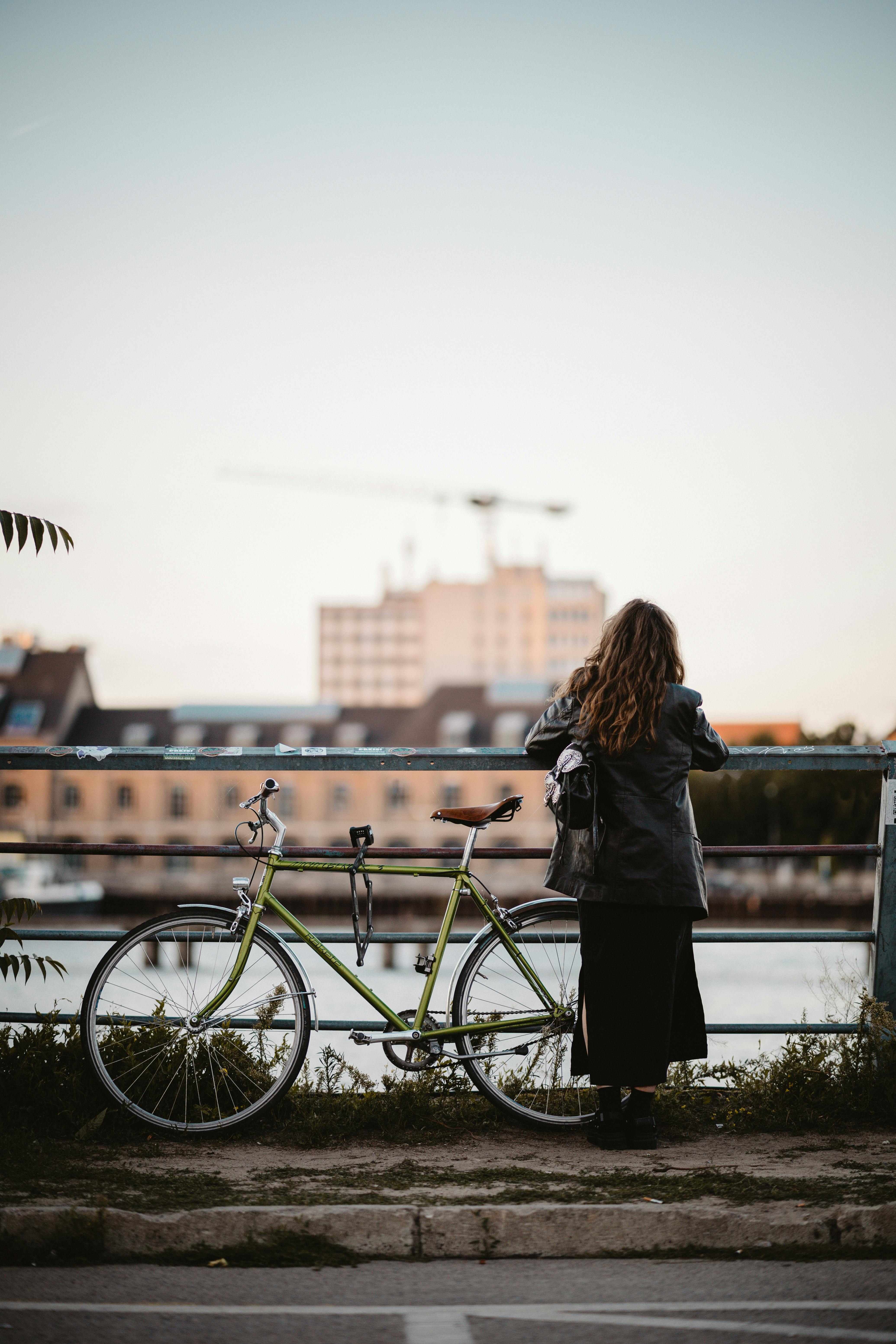 A woman stands next to a bicycle, gazing at the Berlin cityscape over a river during daytime.