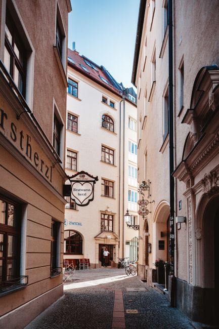 Explore the charming narrow alleyways of Munich, showcasing historic buildings and cozy restaurant settings.