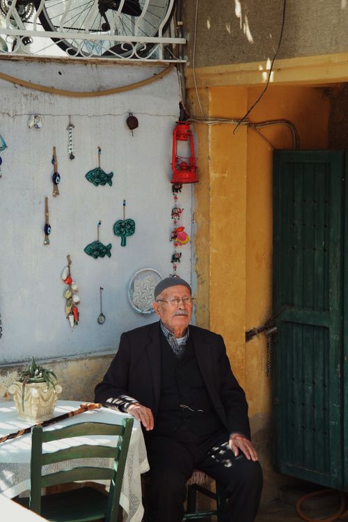 Free Senior man sitting in a vibrant courtyard with wall decorations and oil lamp. Stock Photo