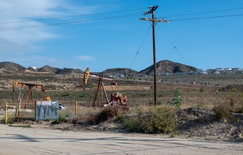 Free Oil pump jacks operating in a rural landscape with utility poles and hills in the background. Stock Photo