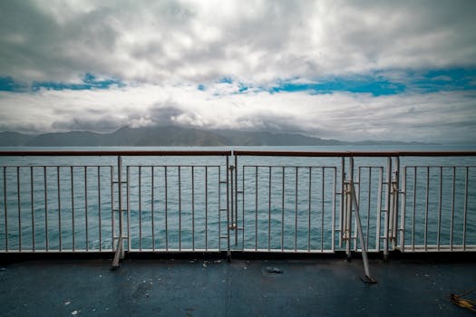 A tranquil ocean view with railings, clouds, and distant mountains, captured from a ferry in Wellington.