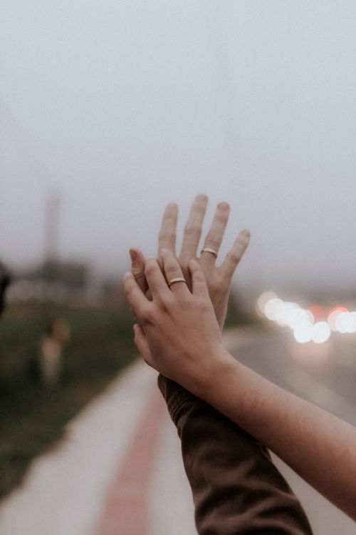 Free Close-up of a couple's hands with rings, raised together against an urban outdoor backdrop. Stock Photo