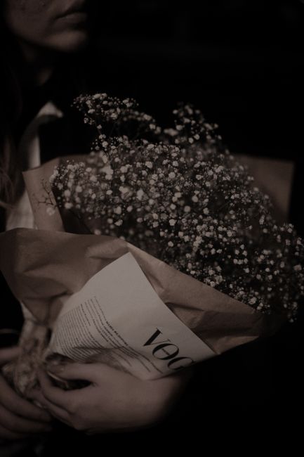 A woman holding a sepia-toned bouquet wrapped in paper, creating a classic and moody atmosphere.