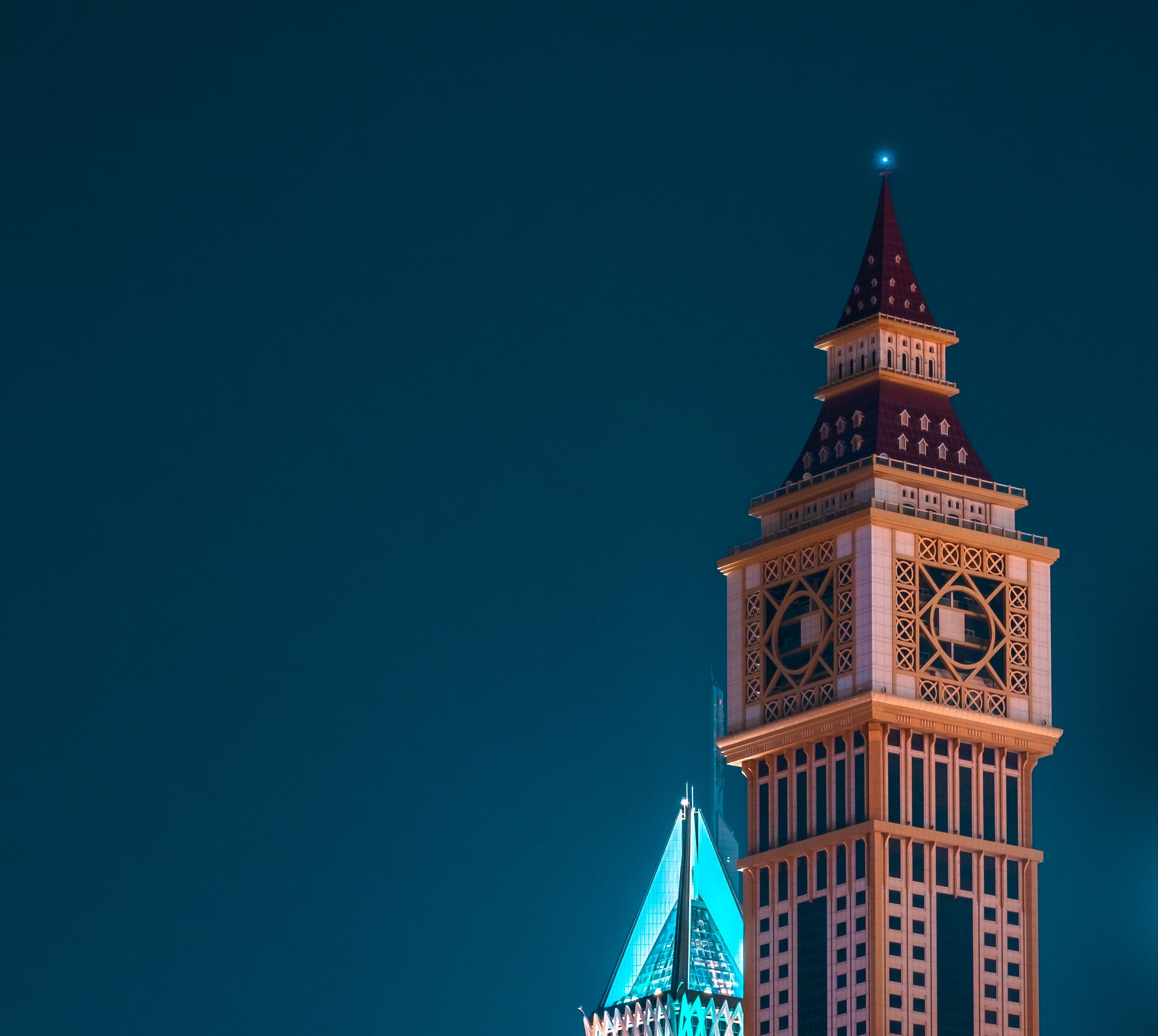 A modern clock tower against a night sky, illuminated in a vibrant cityscape.