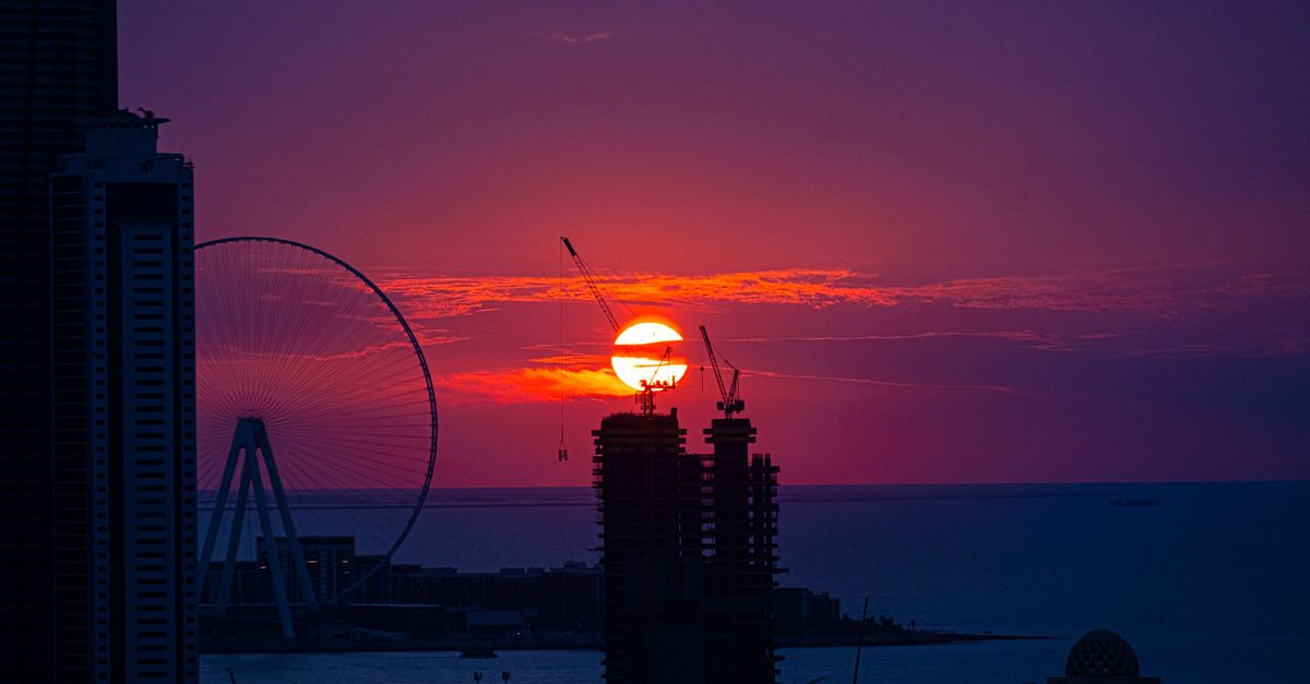 A breathtaking sunset over a city with a silhouetted Ferris wheel and construction cranes.