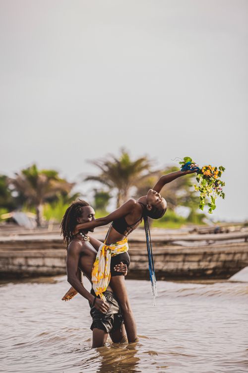 Free A couple embraces and dances in water, holding a flower bouquet, exuding romance. Stock Photo