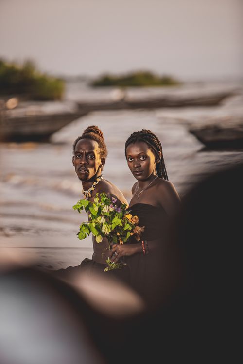 Free A couple sitting on the beach holding flowers, capturing a moment of romance and togetherness. Stock Photo