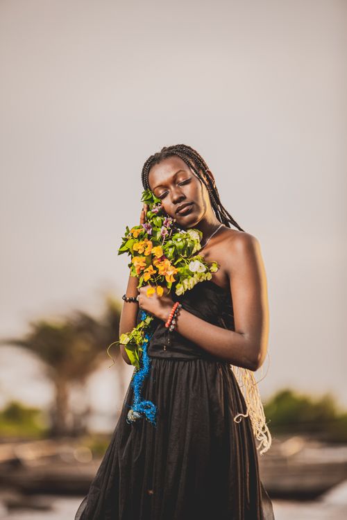 Free Stylish black woman in a flowing black dress embracing vibrant flowers outdoors. Stock Photo