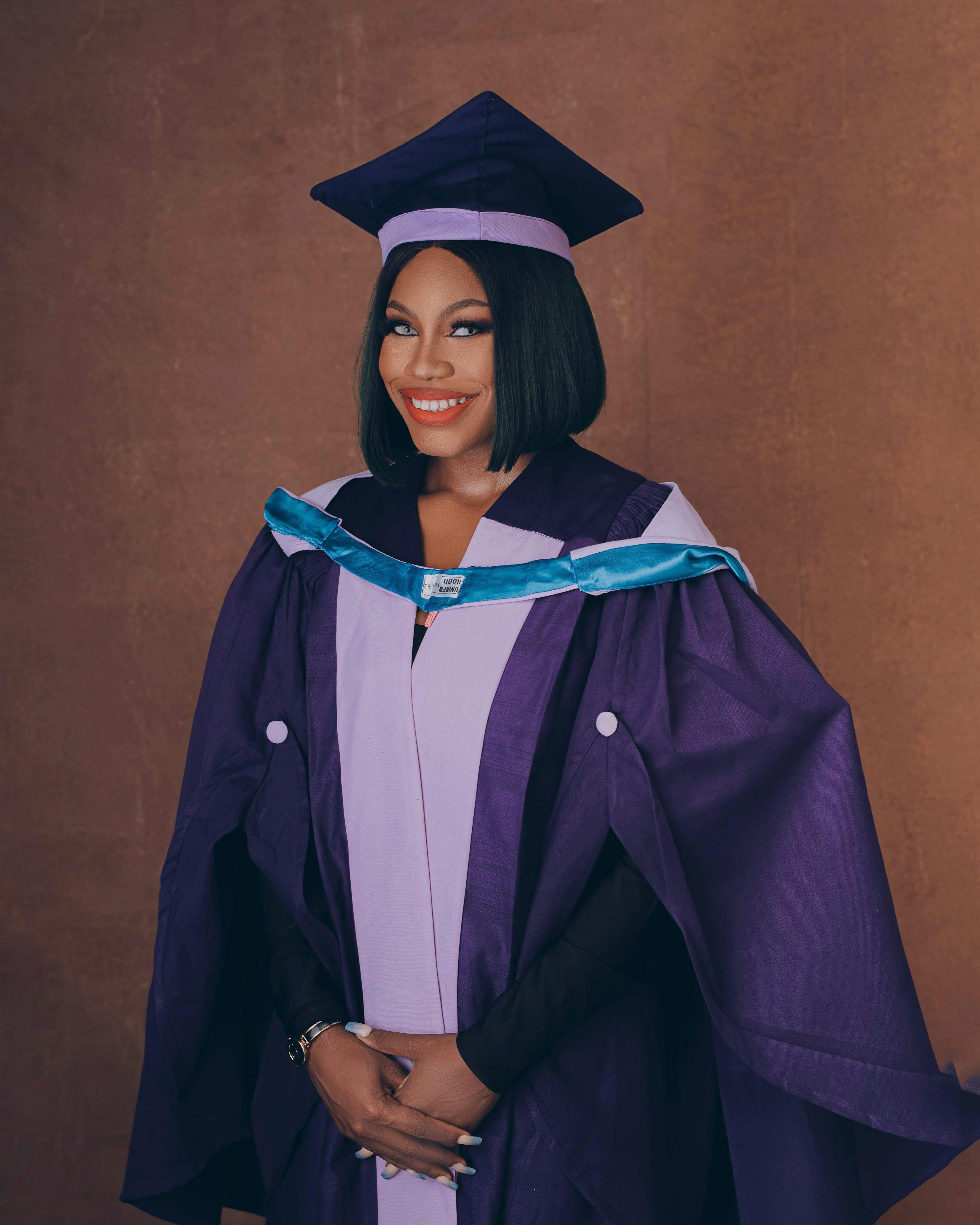 Smiling woman in graduation gown and cap in a studio setting.