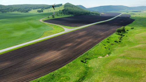 Free A stunning aerial panorama displaying lush green and freshly plowed fields divided by a road in a rural landscape. Stock Photo