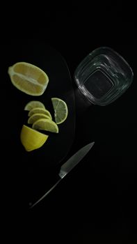 Sliced lemons with a knife and glass on black background create a dramatic food still life.