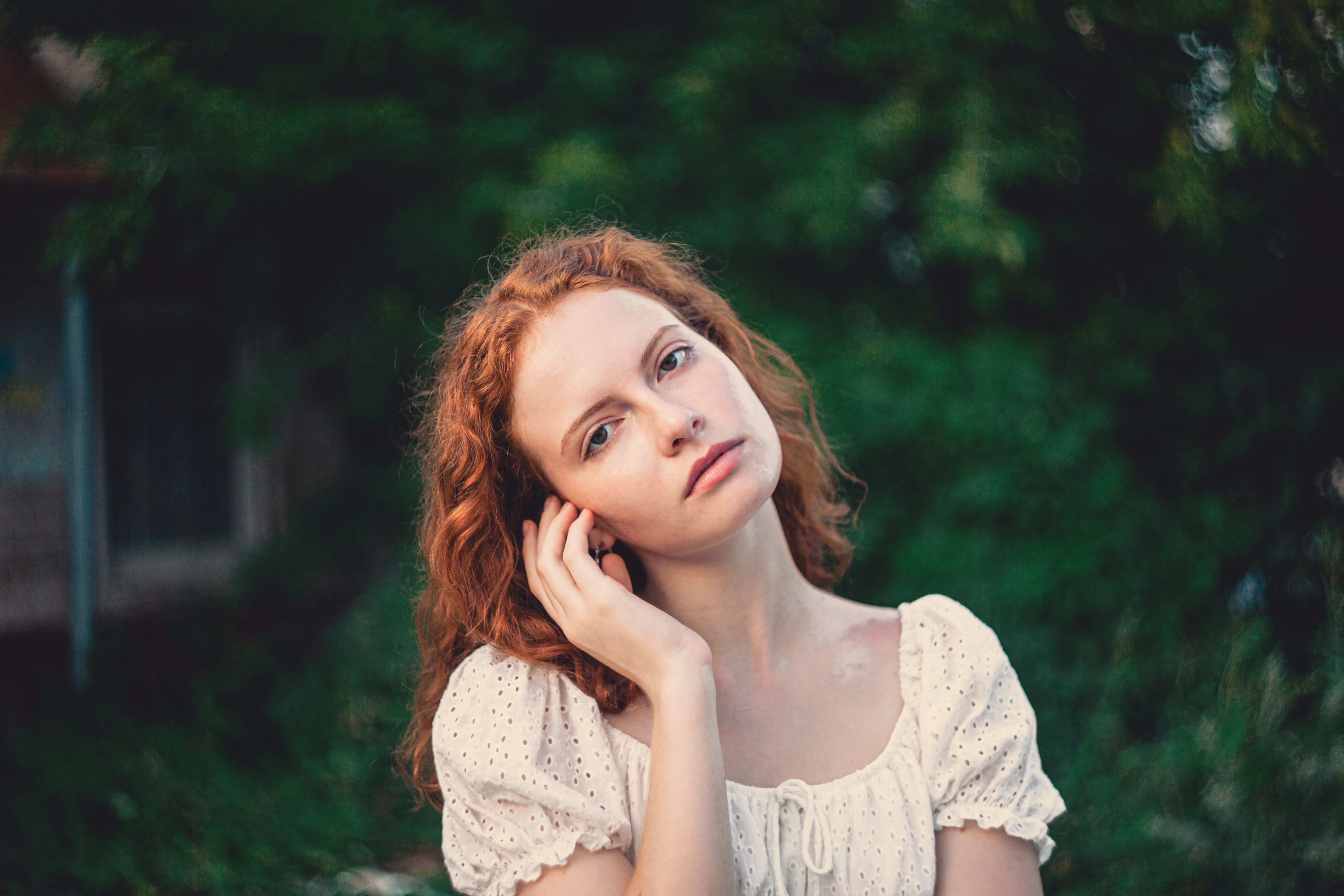 Young woman with red hair posing outdoors in a garden setting.