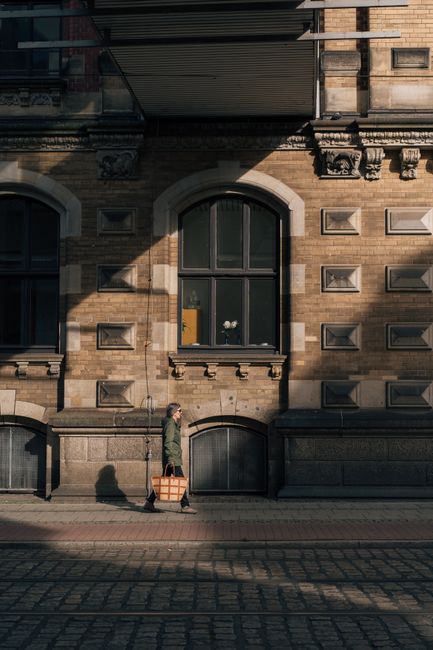 A woman walks with a bag on a sunlit sidewalk in Bremen, Germany, showcasing urban architecture.