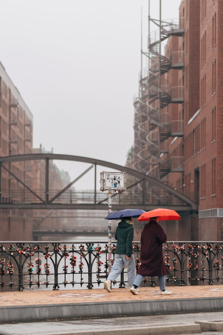 People With Umbrellas Walking On City Bridge