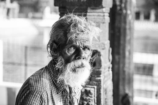 黑白肖像中，一位长着胡须的老人置身于户外城市环境