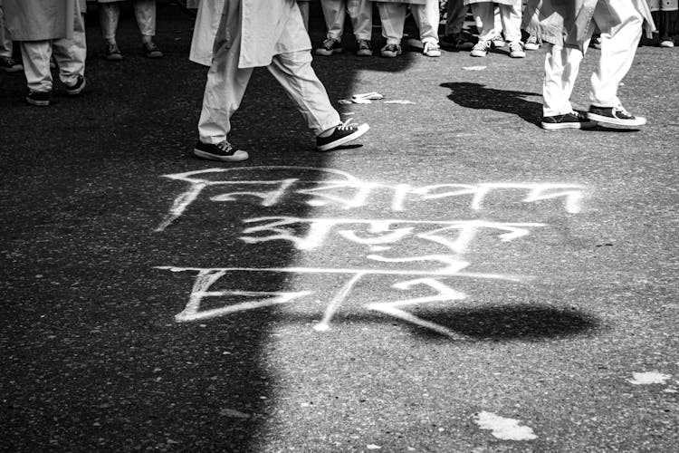 Legs Of People Walking On Pavement Near Chalk Writing