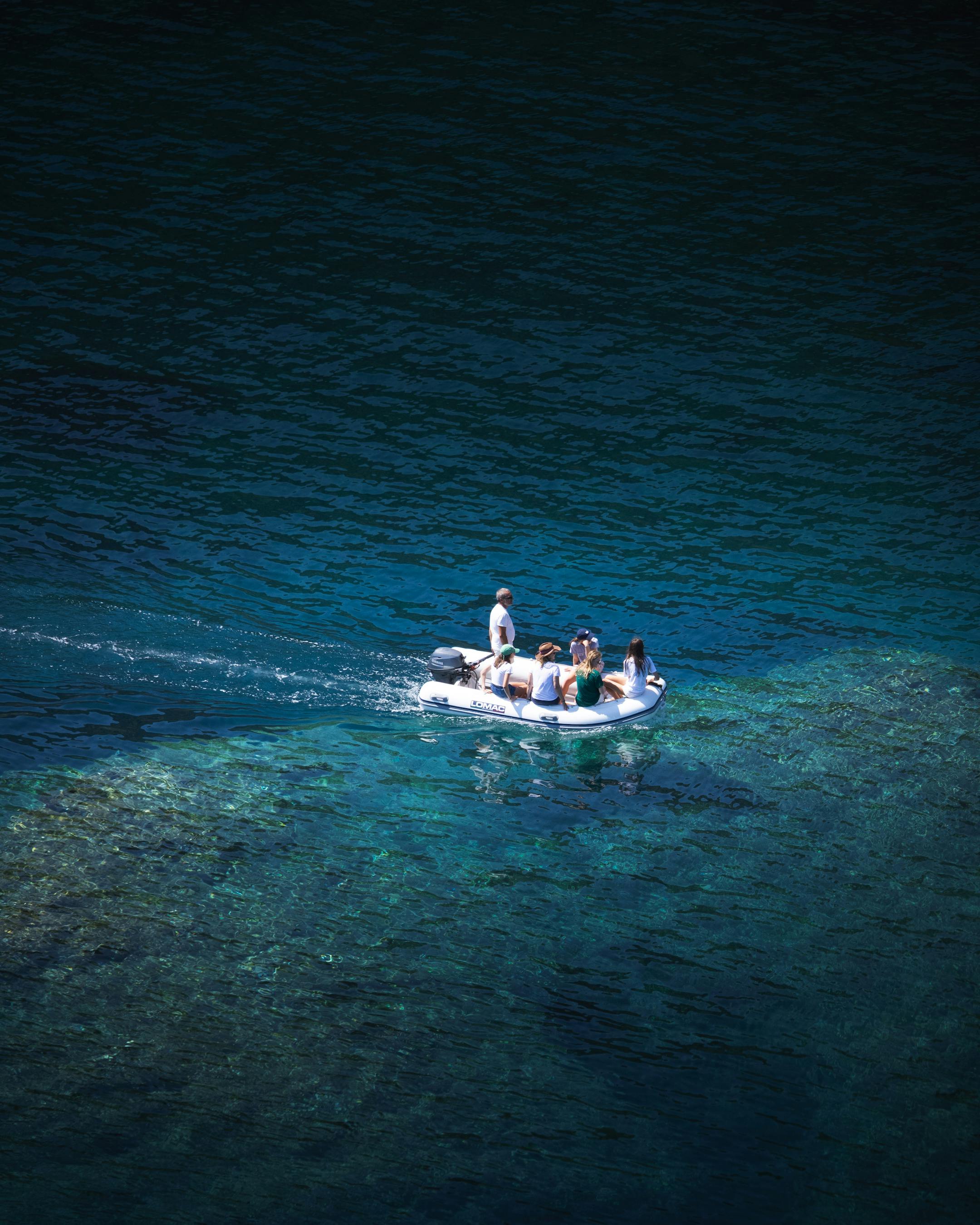 Drone shot of a small boat with people on crystal-clear blue lake water.