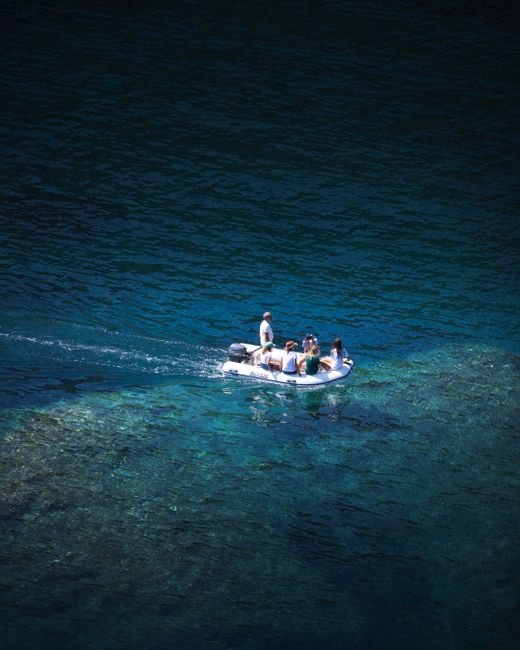 Drone shot of a small boat with people on crystal-clear blue lake water.