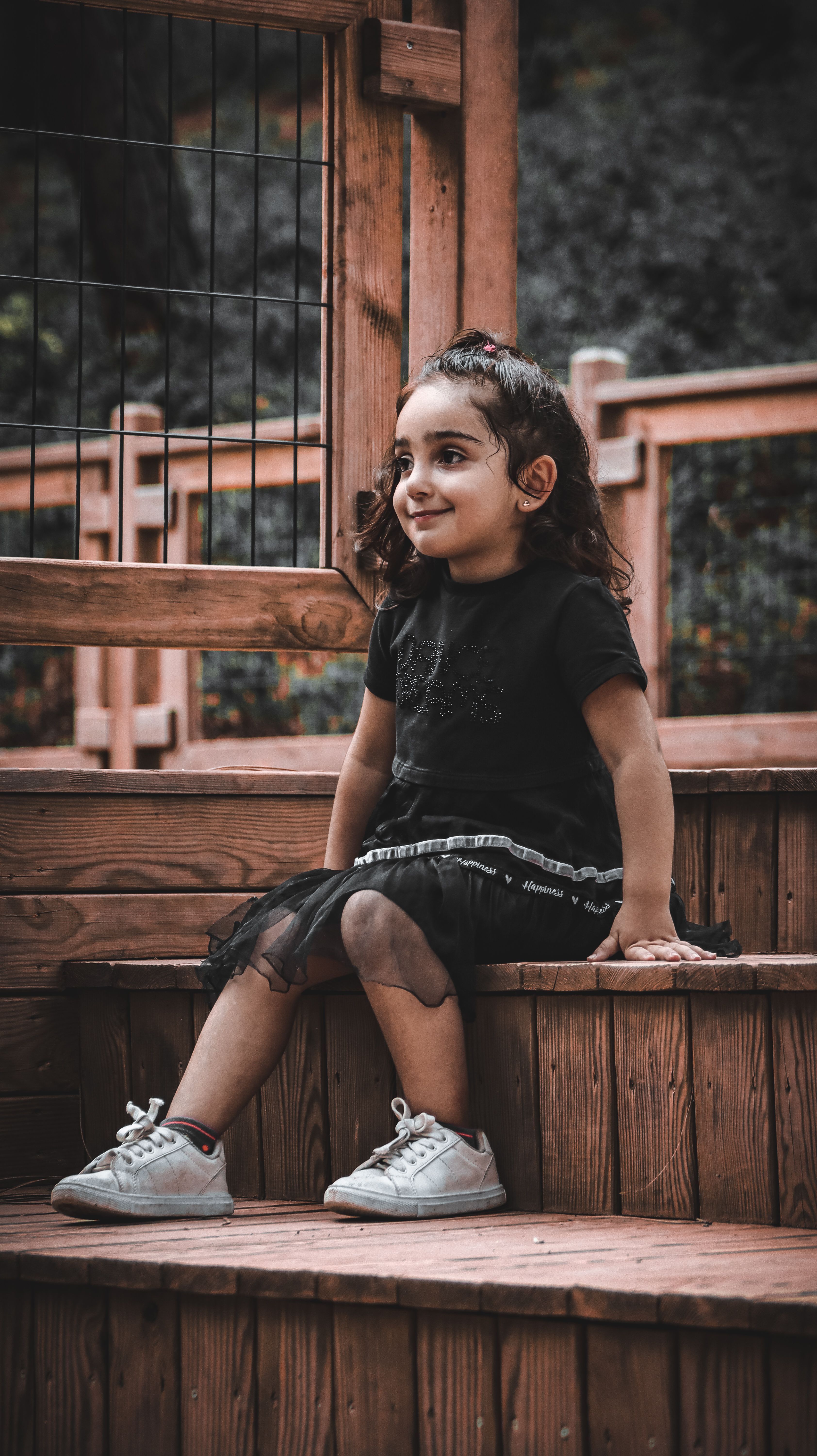 Cute Little Girl in Black Dress Sitting on Wooden Stairs · Free Stock Photo