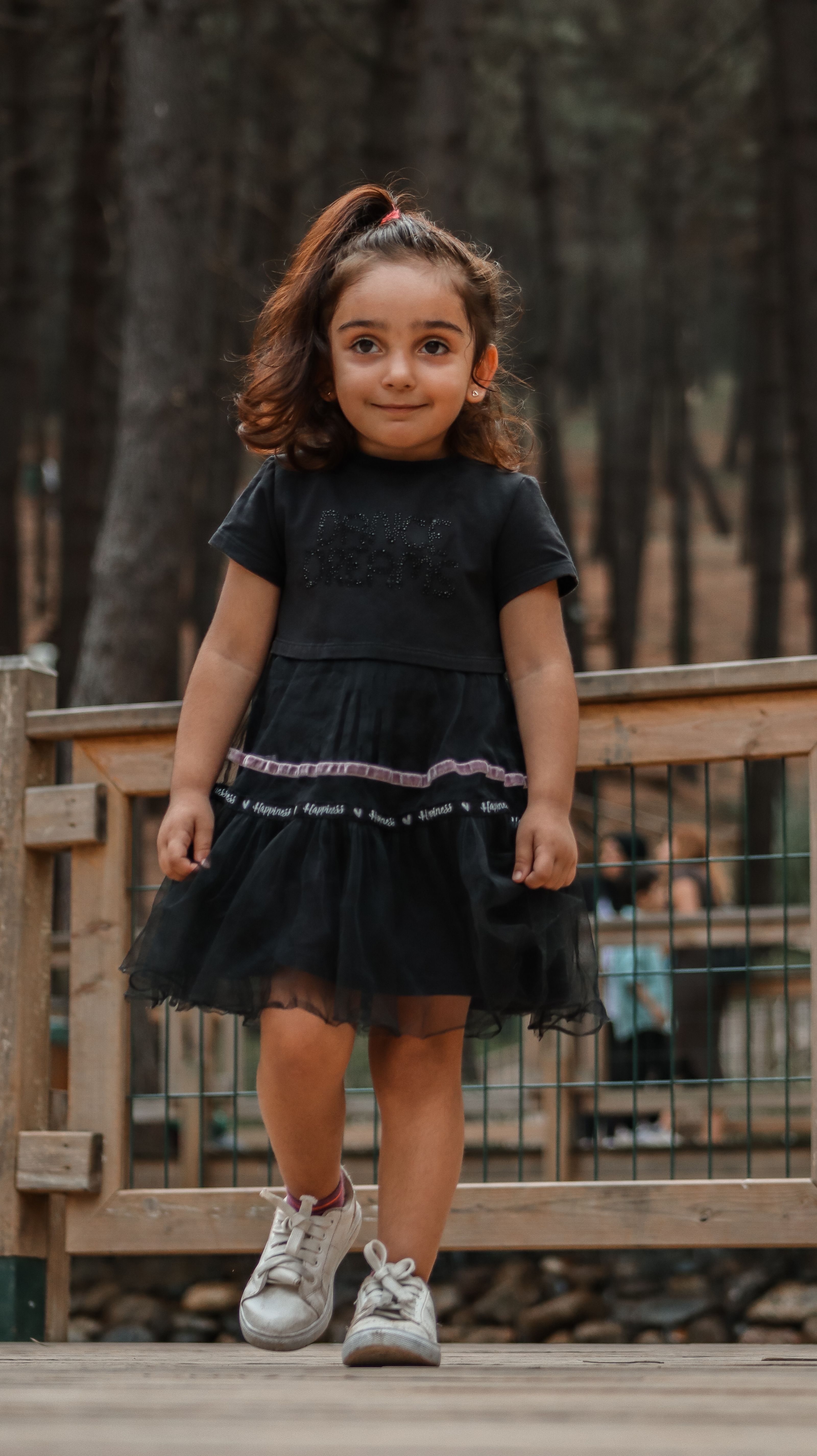 Menina fofa caminhando em uma floresta vestindo um vestido preto estiloso e tênis.
