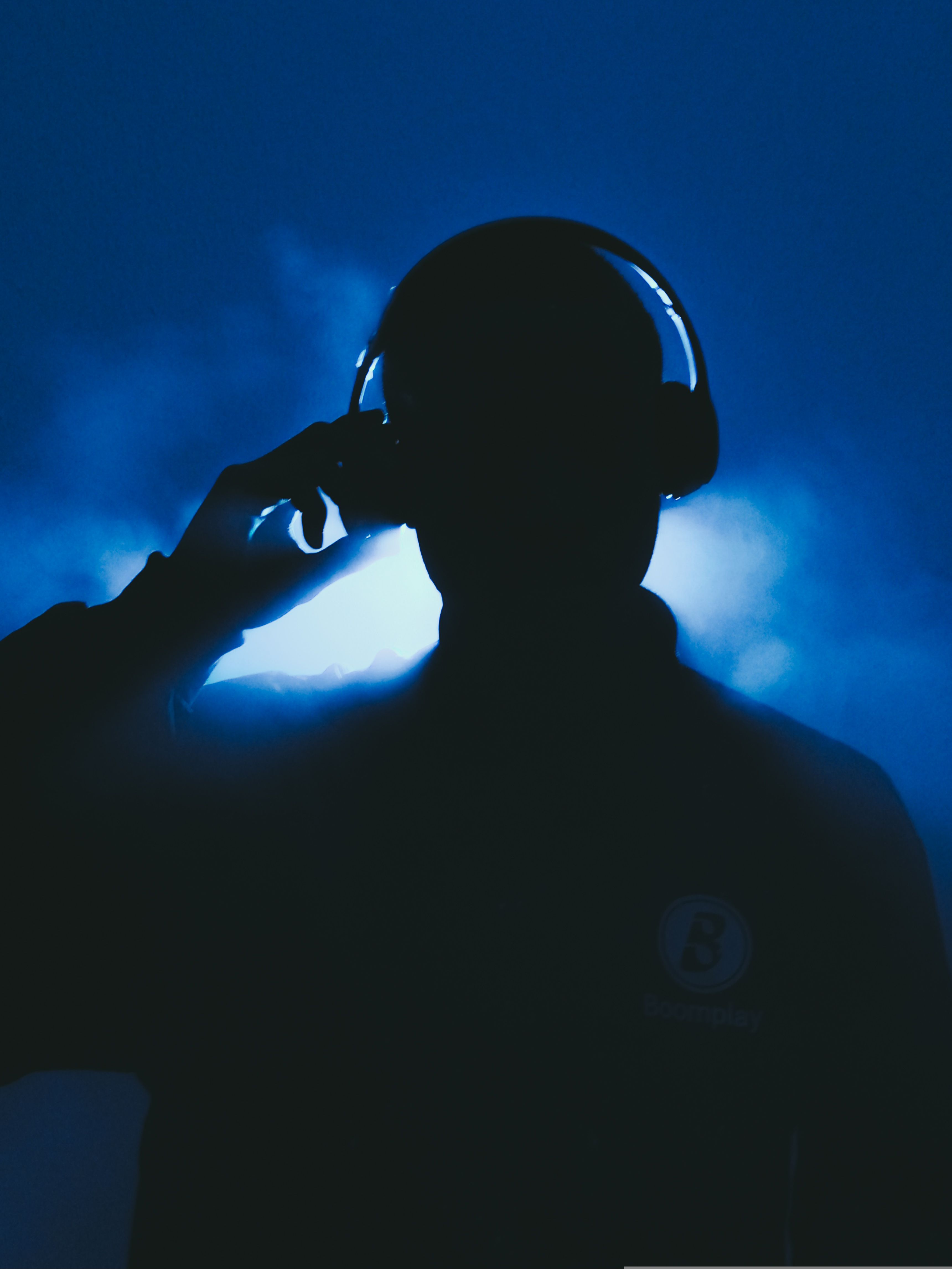 Silhouette of a man wearing headphones, backlit with blue lighting and mysterious smoke.
