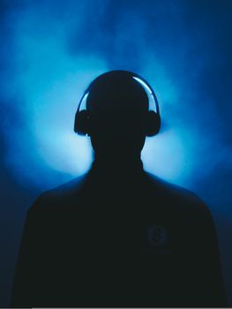 Artistic silhouette of a person wearing headphones in a blue smoky setting, evoking mystery.
