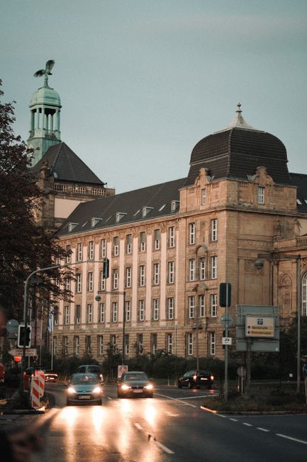 Street view of a historic building in Düsseldorf, Germany, captured at dusk with cars passing by.