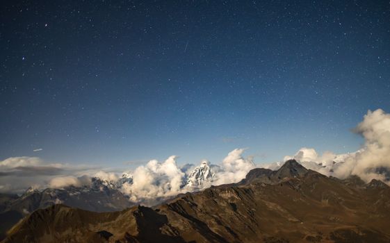A breathtaking view of the Matterhorn under a starry night sky, enveloped by clouds.