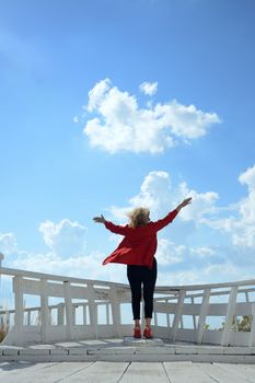 Back view of a woman with arms raised, enjoying a clear blue sky.