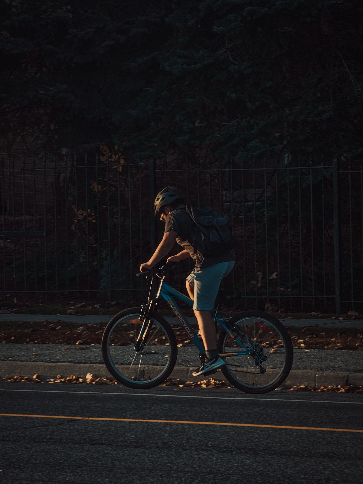 Helmeted cyclist with a backpack riding through the city at dusk