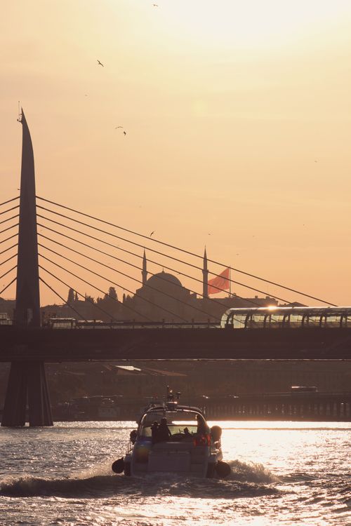 Free Scenic view of a motorboat passing under Halic Bridge at sunset in Istanbul, highlighting the city's iconic skyline. Stock Photo