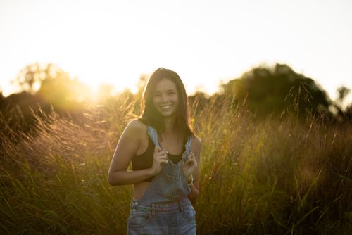 Free A woman with long brunette hair smiling in a grassy field at sunset. Stock Photo