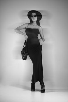 Chic portrait of a woman in a black dress, hat, and sunglasses with a fashionable vibe.