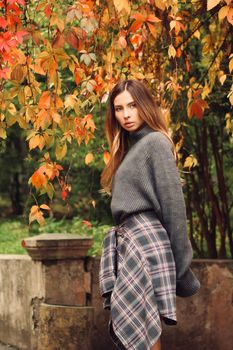 Elegant woman in fashionable outfit stands amidst vibrant fall foliage in a serene park.