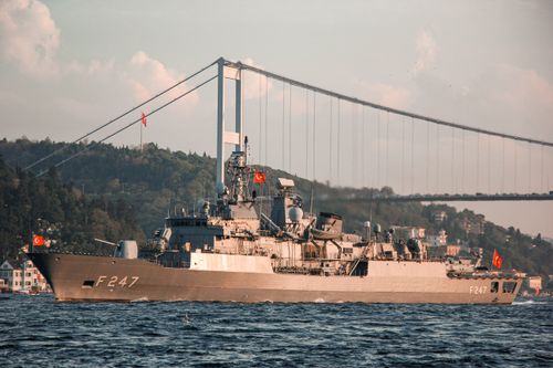 Free Military vessel with Turkish flags sailing under the Bosphorus Bridge in daylight. Stock Photo