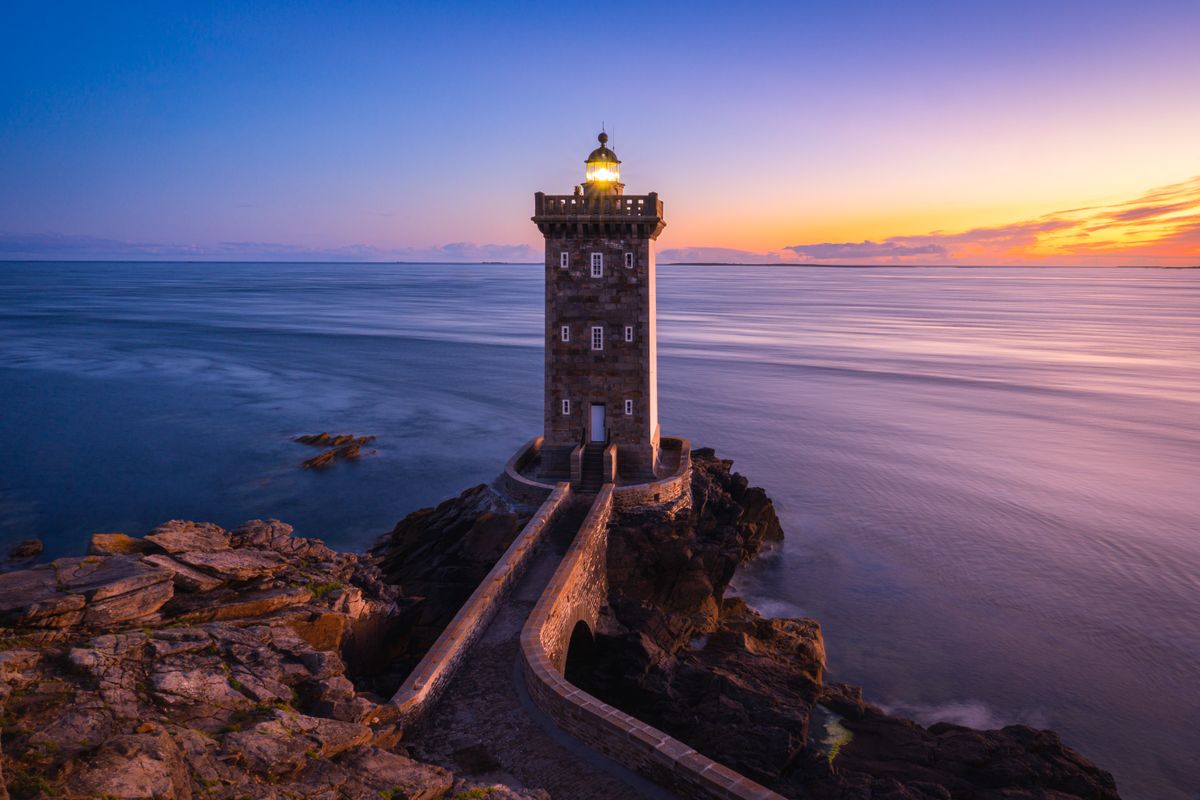 The Kermorvan lighthouse lit at sunset over a smooth sea
