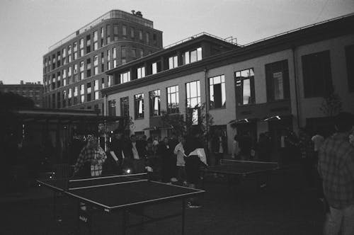 People Standing around Tables for Table Tennis in Black and White