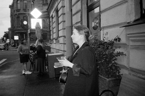 Woman in Coat Standing with Glass on Sidewalk