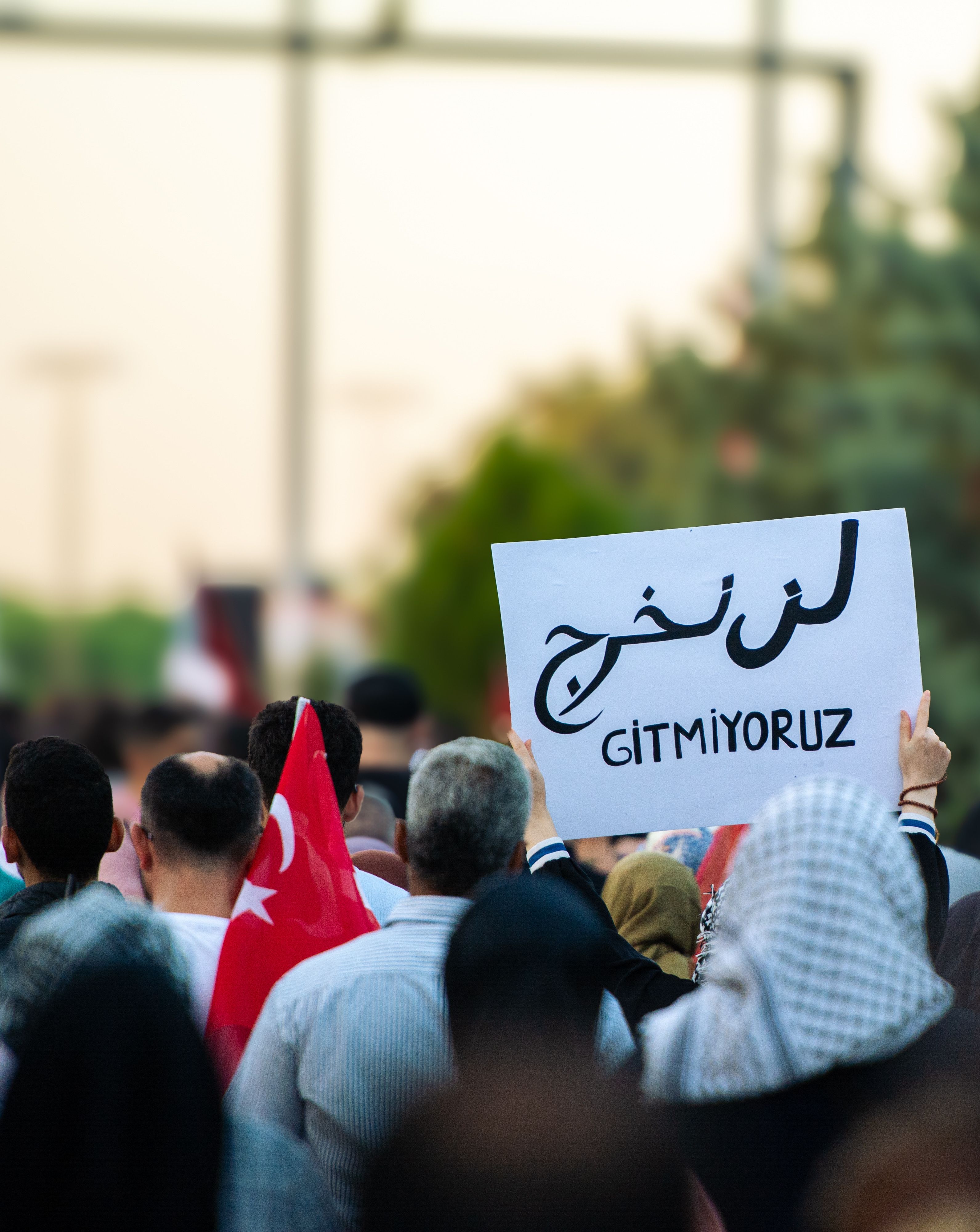A crowd of people at a demonstration holding signs with text and a Turkish flag.