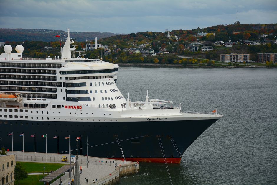 The iconic Queen Mary 2 cruise ship docked at a beautiful harbor with scenic city views.